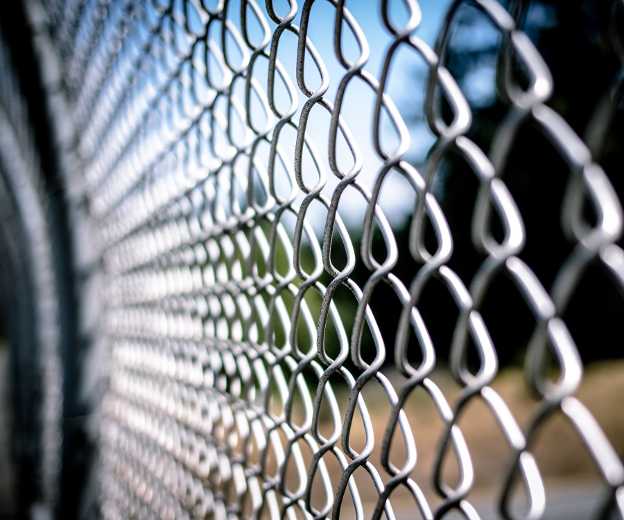 Perspektywiczne zbliżenie na siatkę ogrodzeniową ocynkowaną z widocznym tłem nieba i zieleni.