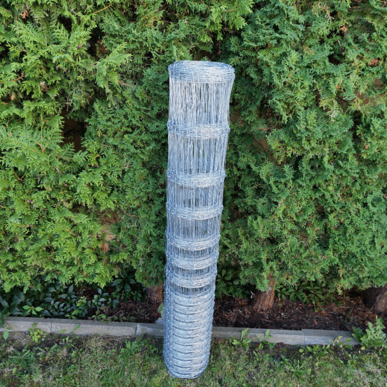 Siatka leśna zwinięta w rolkę, ustawiona przy żywopłocie.